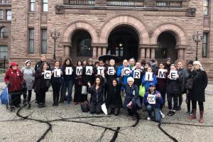 "volunteers holding letter spelling Climate Crime outside Queens' Park"